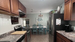 A kitchen with wooden cabinets, a stainless steel refrigerator, a stove, and a dining area with blue chairs and a table. - SASSA MERMAID WATERFRONT HOUSE WITH KAYAKS AND POOL (Homosassa)