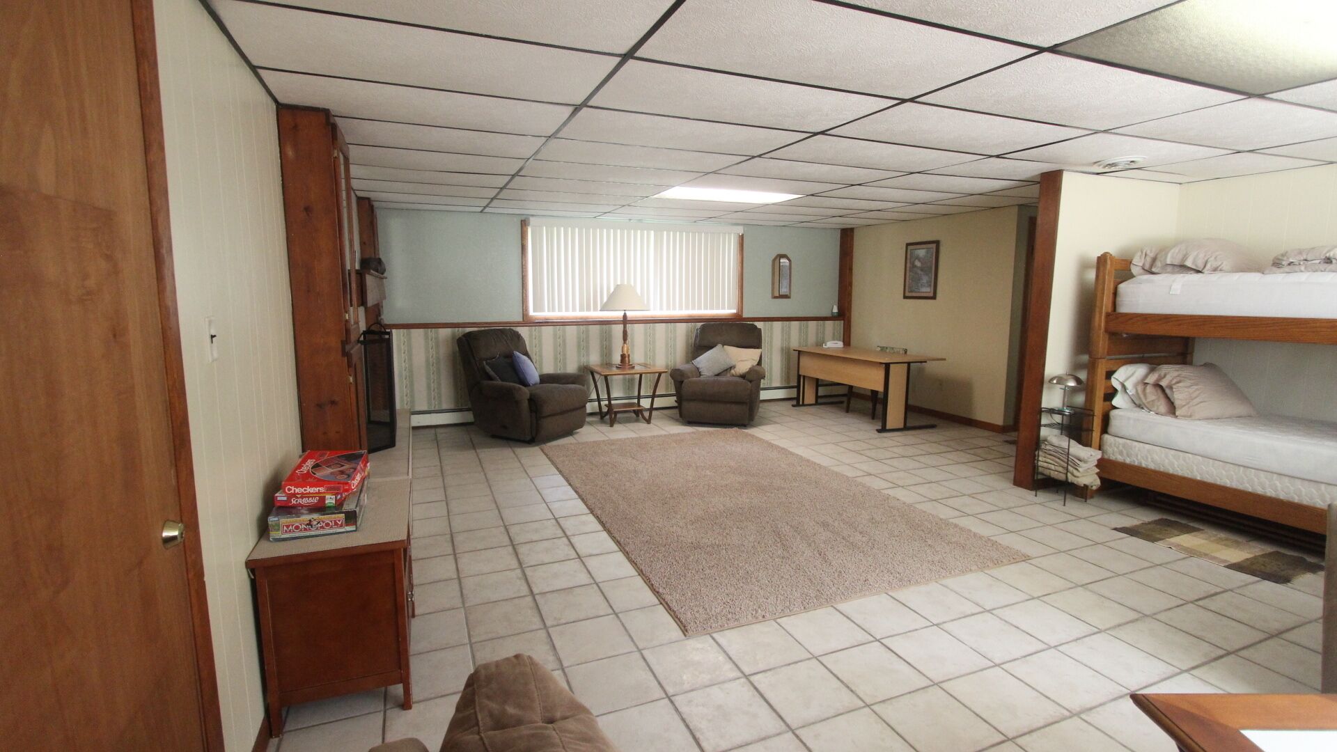 A compact room with a bunk bed, two armchairs, a small table, and a window with blinds.