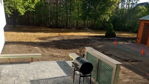 A patio with a barbecue grill, stone flooring, and a wooden bench.