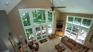 A spacious living room with a large window, a ceiling fan, and a sofa. - Modern Lakefront Retreat Sleeps 13, a 4-Season Getaway 2 Hours from Chicago (decatur)