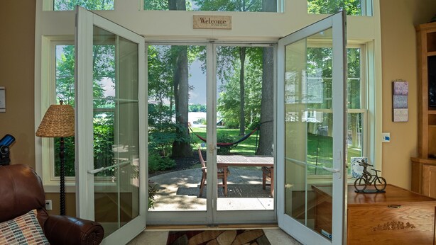 A room with a large glass door leading to a patio with a hammock, a wooden table, and chairs. - Modern Lakefront Retreat Sleeps 13, a 4-Season Getaway 2 Hours from Chicago (decatur)