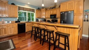 A kitchen with wooden cabinets, a refrigerator, a microwave, and bar stools. - Modern Lakefront Retreat Sleeps 13, a 4-Season Getaway 2 Hours from Chicago (decatur)
