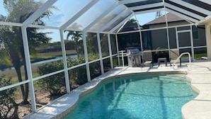 Ein Pool mit überdachter Terrasse, inklusive Grill und Sitzgelegenheiten.