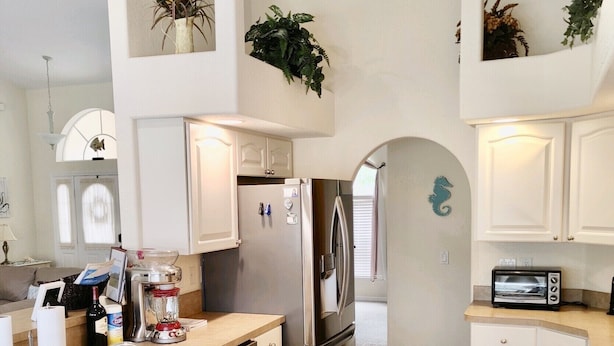 Eine moderne Küche mit weißen Schränken, einem Edelstahlkühlschrank, einem eingebauten Ofen und einer Mikrowelle. Es gibt einen Deckenventilator, eine kleine Kücheninsel mit Spüle sowie eine Spritzschutzleiste mit einem dekorativen Seepferdchen.