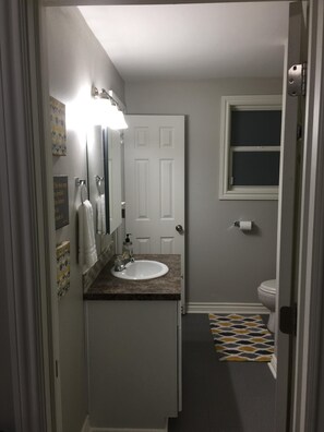 A narrow bathroom with a white sink, a mirror, and a towel rack. - Historically Modern Delano (Wichita)