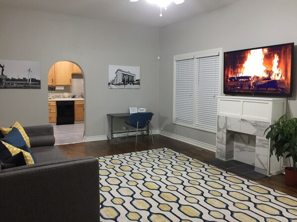 A living room with a sofa, a TV, a fireplace, and a kitchen in the background. - Historically Modern Delano (Wichita)