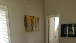 A bedroom with a large bed, a wooden bench with towels, a painting on the wall, and a TV mounted on the wall. - Historically Modern Delano (Wichita)