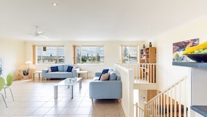 A spacious living room with two sofas, a coffee table, and a bookshelf. Large windows offer a view of the neighborhood. - Ocean View Anna Bay, 23 Ocean Avenue (Anna Bay)