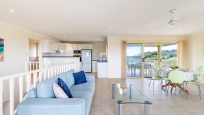 A modern living room with a light blue sofa, a glass coffee table, and a balcony with a table set for dining. - Ocean View Anna Bay, 23 Ocean Avenue (Anna Bay)