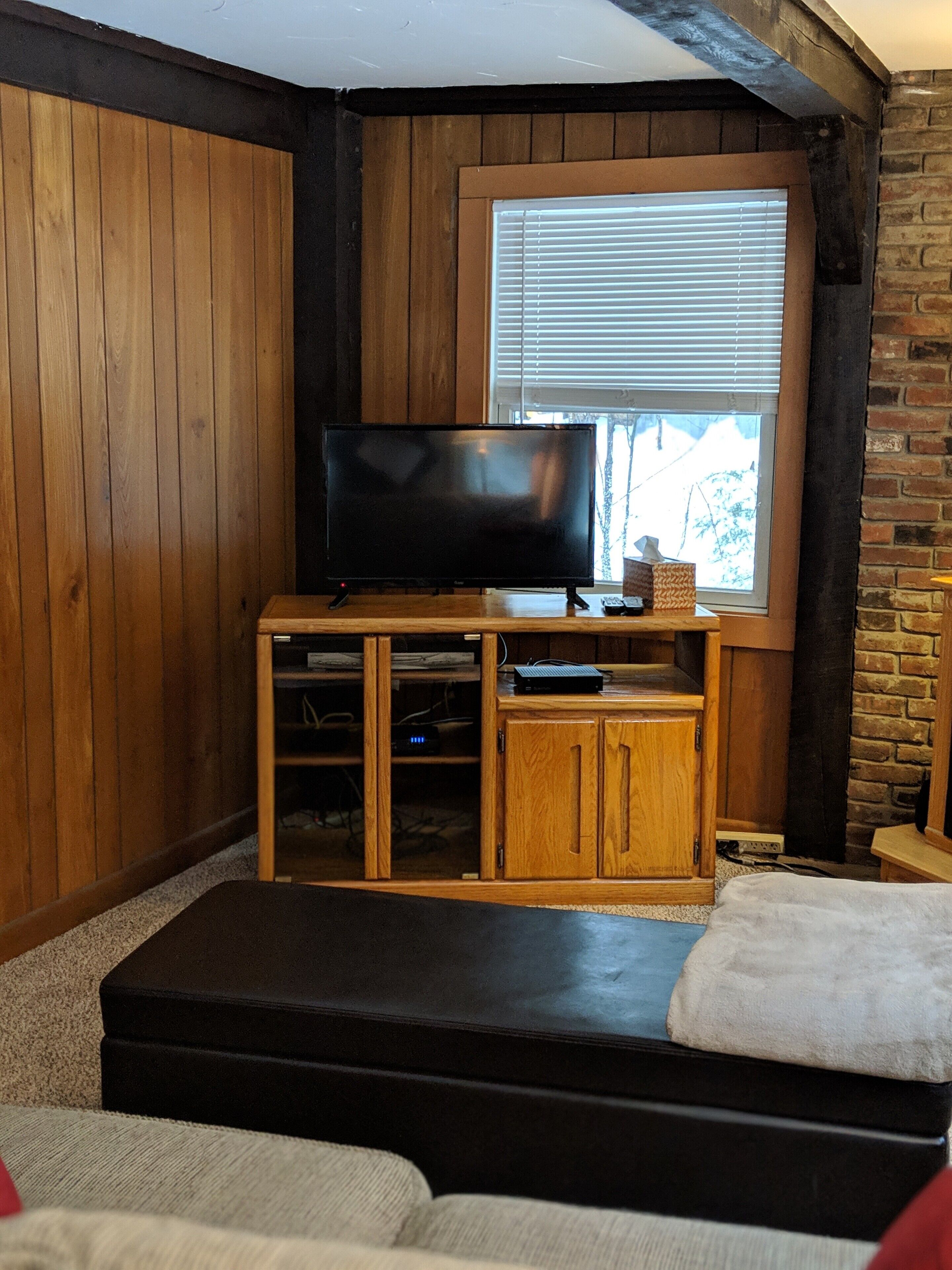 Una sala de estar acogedora con un televisor de pantalla plana sobre un pedestal de madera, una chimenea y una ventana con persianas.