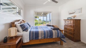 Un dormitorio con cama, cómoda de madera, mesita de noche, ventilador de techo y ventana con vistas al exterior.