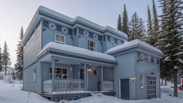 Une maison à deux étages, dotée d’un porche et d’un garage, entourée de neige et d’arbres.