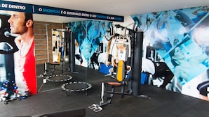Ein Fitnessstudio mit verschiedenen Trainingsgeräten, darunter ein Laufband, Kraftgeräte und eine Trampolin.