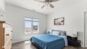 Un dormitorio con una cama, ventilador de techo, ventana, mesita de noche y cómoda.