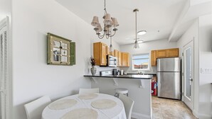 Una cocina moderna con armarios blancos, un refrigerador de acero inoxidable, un comedor con una mesa y sillas blancas, y una araña.
