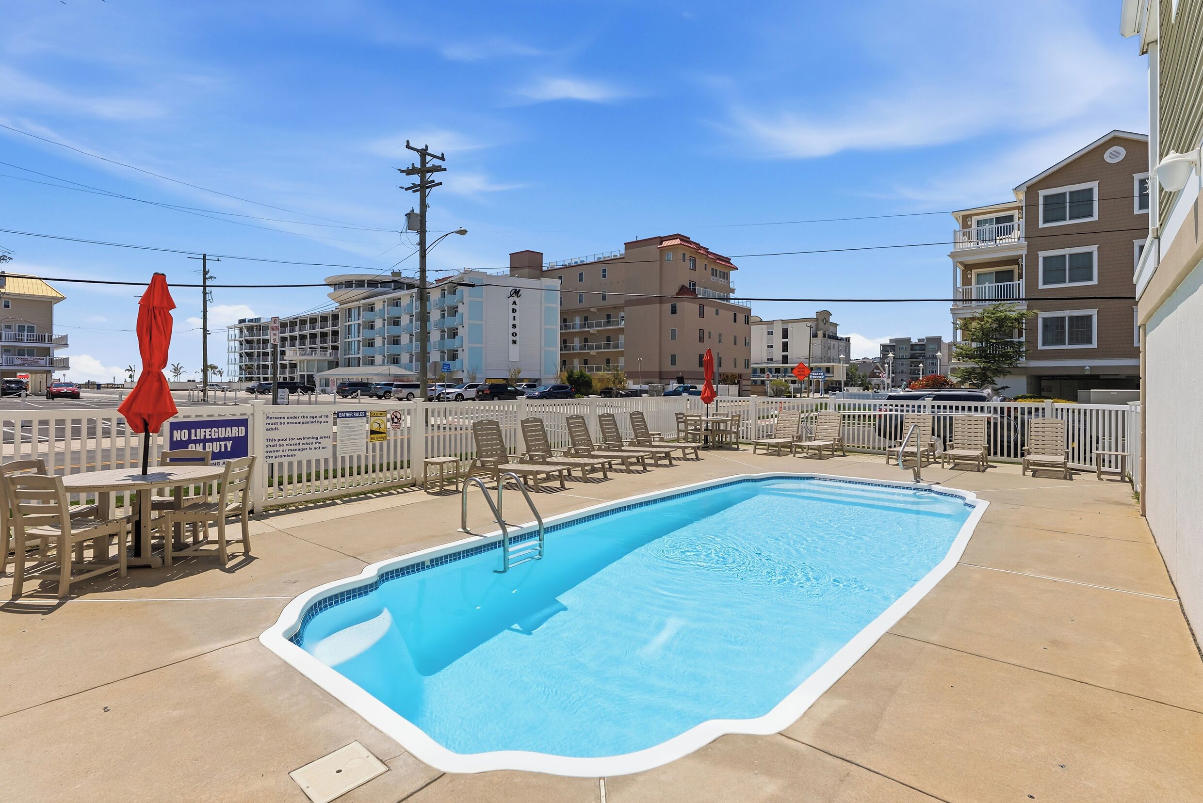 A swimming pool with a no lifeguard on duty sign, lounge chairs, and a view of buildings in the background.