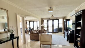 Ein geräumiges Wohnzimmer mit einer Couch, einem Couchtisch und einem Fernseher. Im Hintergrund ist ein Essbereich mit Tisch und Stühlen zu sehen.