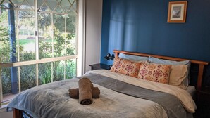 A bedroom with a large window, a bed with a grey blanket, floral pillows, and a wooden headboard.