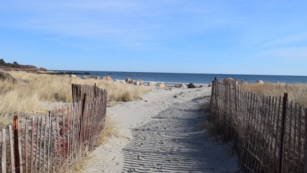 Un sendero arenoso que conduce a la playa, bordeado por vallas de madera.