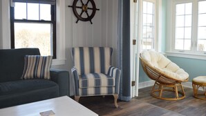 Una habitación con un sillón a rayas, una silla de ratán, un sofá verde oscuro y una mesa de centro blanca.