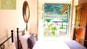 A bedroom with a bed, pillows, a mirror, and a view of a garden through an open door. - Luxury Villa Tuscany (Bagni di Lucca)