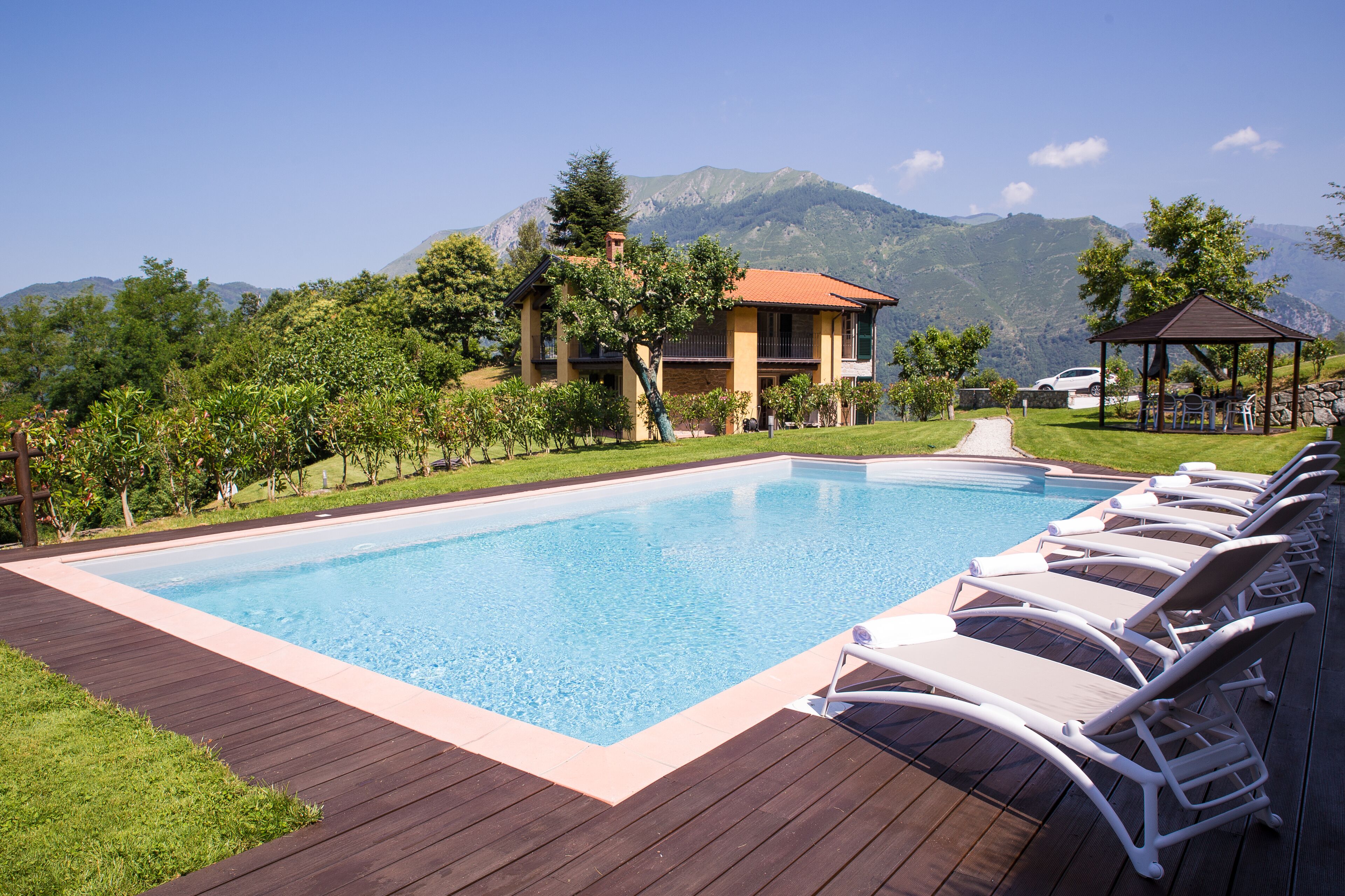 Piscina com espreguiçadeiras, um deck de madeira e montanhas ao fundo.
