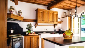 A kitchen with wooden cabinets, a stove, and a bowl of fruit on the counter. - Luxury Villa Tuscany (Bagni di Lucca)