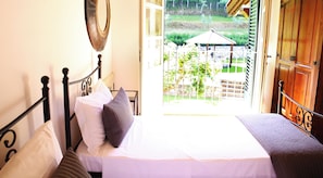 Un dormitorio con cama, almohadas, un espejo y vistas a un jardín a través de una puerta abierta.