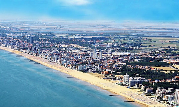 Paesaggio costiero con una lunga spiaggia, una zona urbana densa e un mix di edifici residenziali e commerciali.