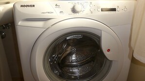 A front-loading washing machine with a control panel, a detergent container on top, and a visible water level indicator.