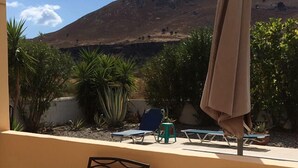 A balcony with a table set for dining, chairs, and an umbrella, overlooking a garden with plants and a hill in the background. - Nineteen 5* reviews. Book 2025 now (Lardos)