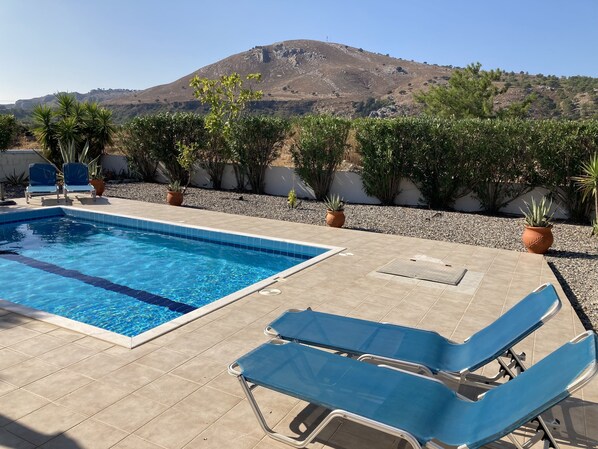 A swimming pool with blue tiles, surrounded by beige tiles and two blue lounge chairs.