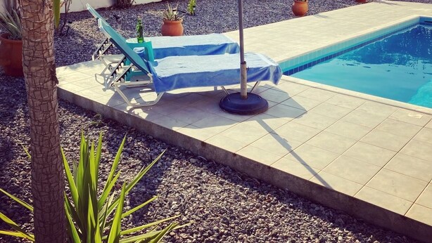 A pool area with a blue lounge chair, an umbrella, and potted plants. - Nineteen 5* reviews. Book 2025 now (Lardos)
