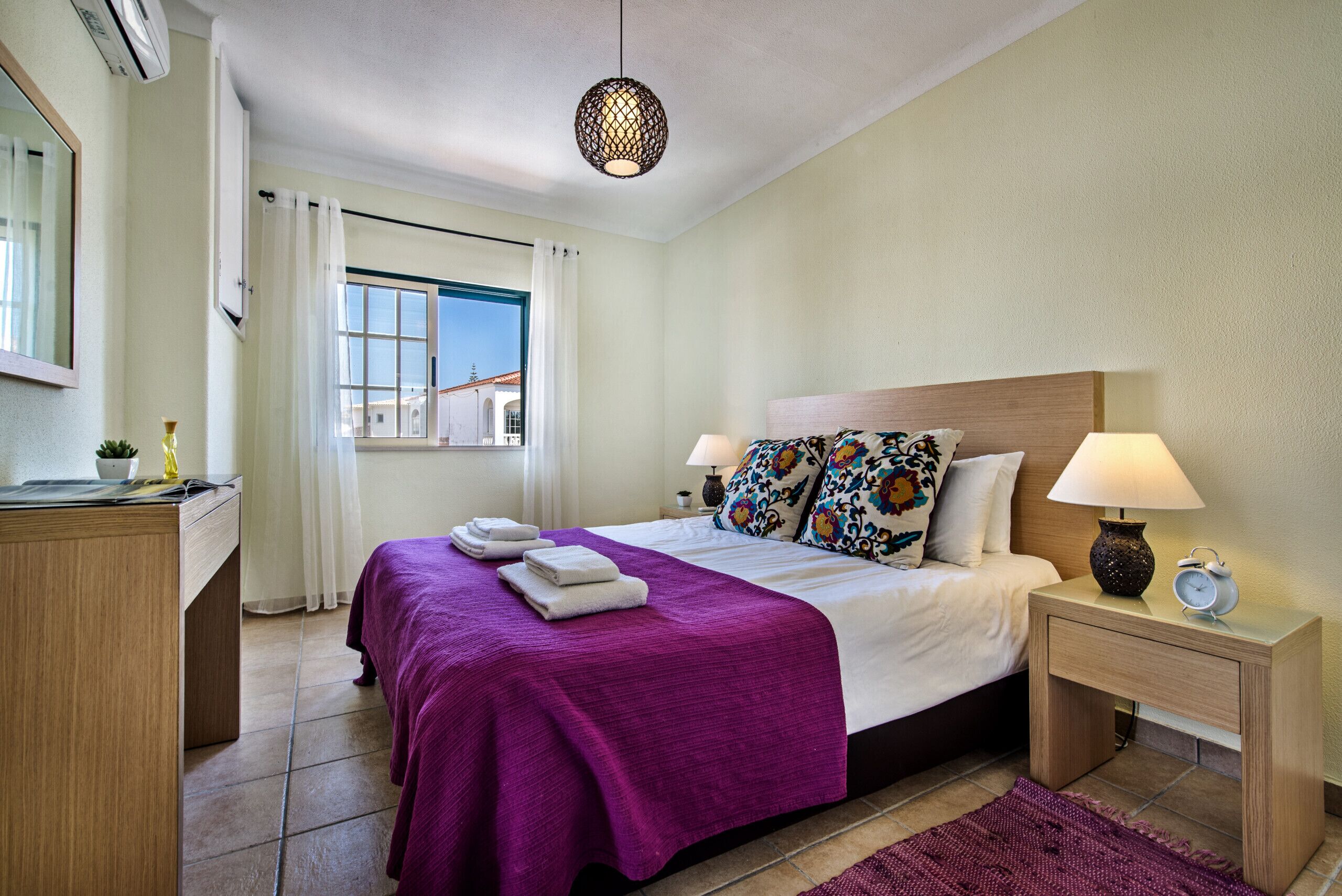 Een netjes ingerichte hotelkamer met een bed, nachtlampjes, een bureau en een raam met gordijnen.