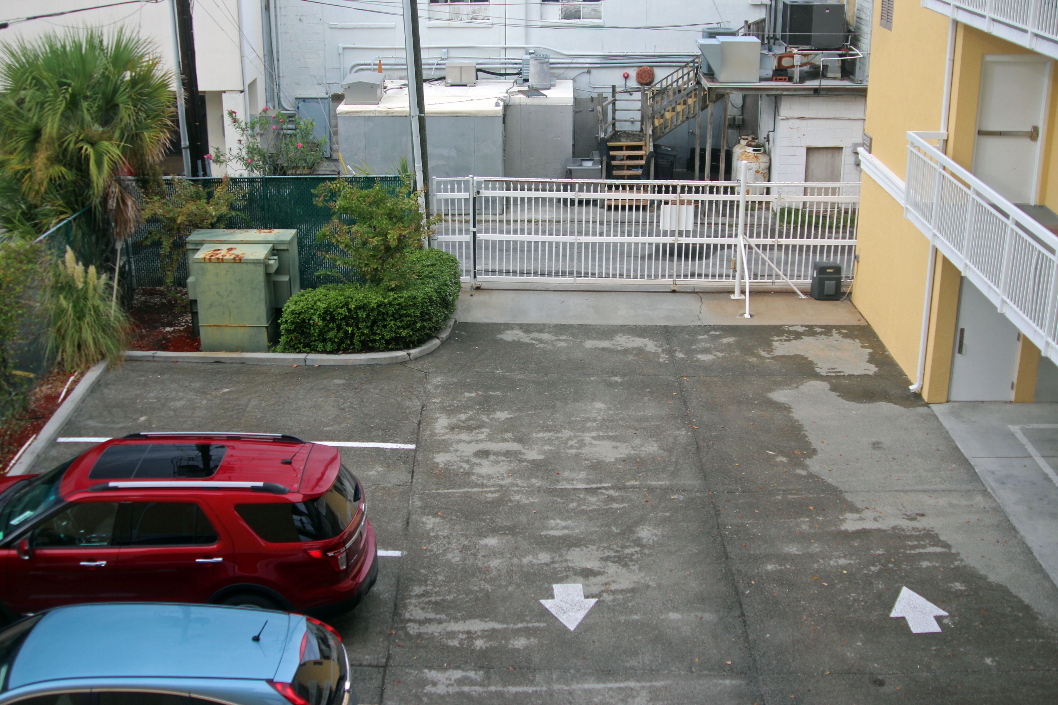 A parking area with two cars, a white fence, and a gated entrance.