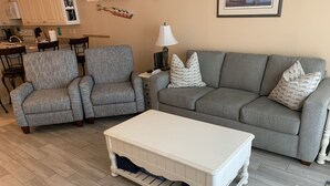 Ein Wohnzimmer mit grauem Sofa, zwei grauen Sesseln, einem weißen Couchtisch und einer Lampe.