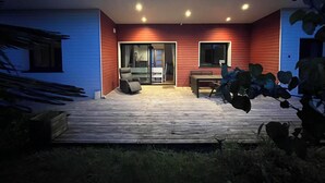 Una casa moderna con terraza de madera, puerta corrediza de vidrio que da a un patio y una pequeña mesa con sillas.