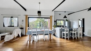 Una cocina moderna con una isla central, un comedor con mesa y sillas, y vistas a zonas verdes.