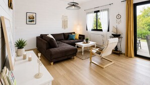 Una sala de estar moderna con un sofá modular, una mesa de centro blanca, un sillón blanco, una mesita auxiliar, una lámpara colgante, un atrapasueños y vistas al verdor a través de una ventana.