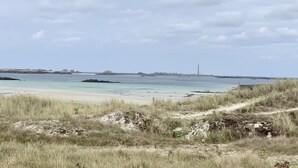 Un paisaje costero con una playa arenosa, dunas cubiertas de hierba y un faro distante.