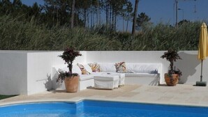 A poolside area with a white sofa set, two potted plants, and a yellow umbrella.