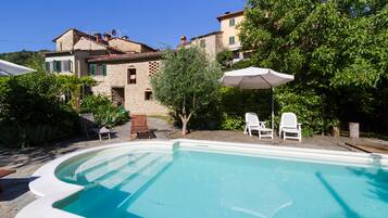 A swimming pool with a stone deck, surrounded by outdoor furniture and a large tree.