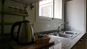 Een keuken met een roestvrijstalen waterkoker, een spoelbak en een raam met zonwering.