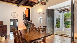 A dining area with a wooden table and chairs, a vase with flowers, a wall clock, and a staircase leading to another room.