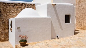 A white-walled building with a stone foundation, a small window, and a potted plant on the ground.