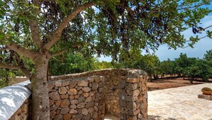 A stone structure with a tree in front, surrounded by a stone-paved area and a clear sky.
