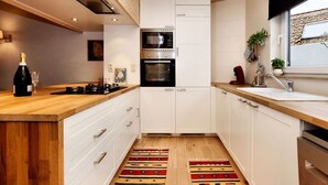 A modern kitchen with white cabinetry, a wooden countertop, a built-in oven, and a window with a view. - Vacation home Martha (Veurne)