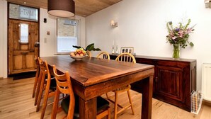 A wooden dining table with chairs, a bowl of fruit, a vase with flowers, and a wooden cabinet. - Vacation home Martha (Veurne)