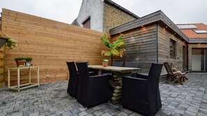 An outdoor patio with a stone-tiled floor, a wooden table with four chairs, and a potted plant. - Vacation home Martha (Veurne)