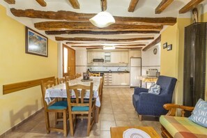 A dining area with a table set for four, wooden chairs, a sofa, and a kitchen in the background.